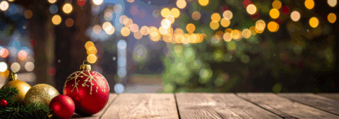 Kerstballen en dennentakken op een houten tafel, met wazige kerstverlichting op de achtergrond.