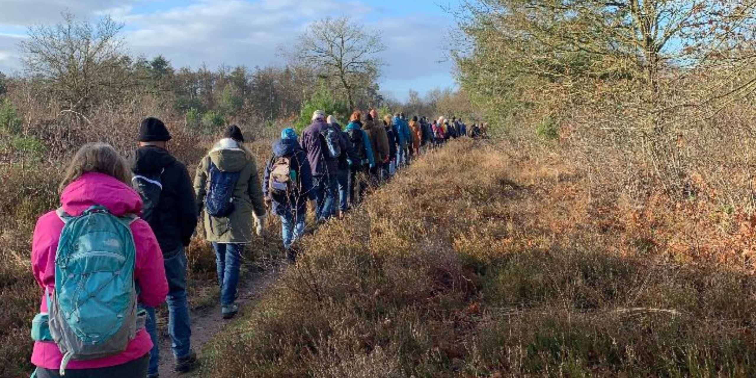 Een groep wandelaars in winterkleding loopt op een smal bospad.