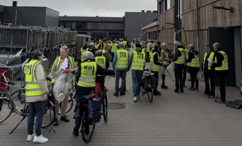 Groep mensen in gele hesjes verzamelt zich voor een schoonmaakactie, met fietsen en grijpers.