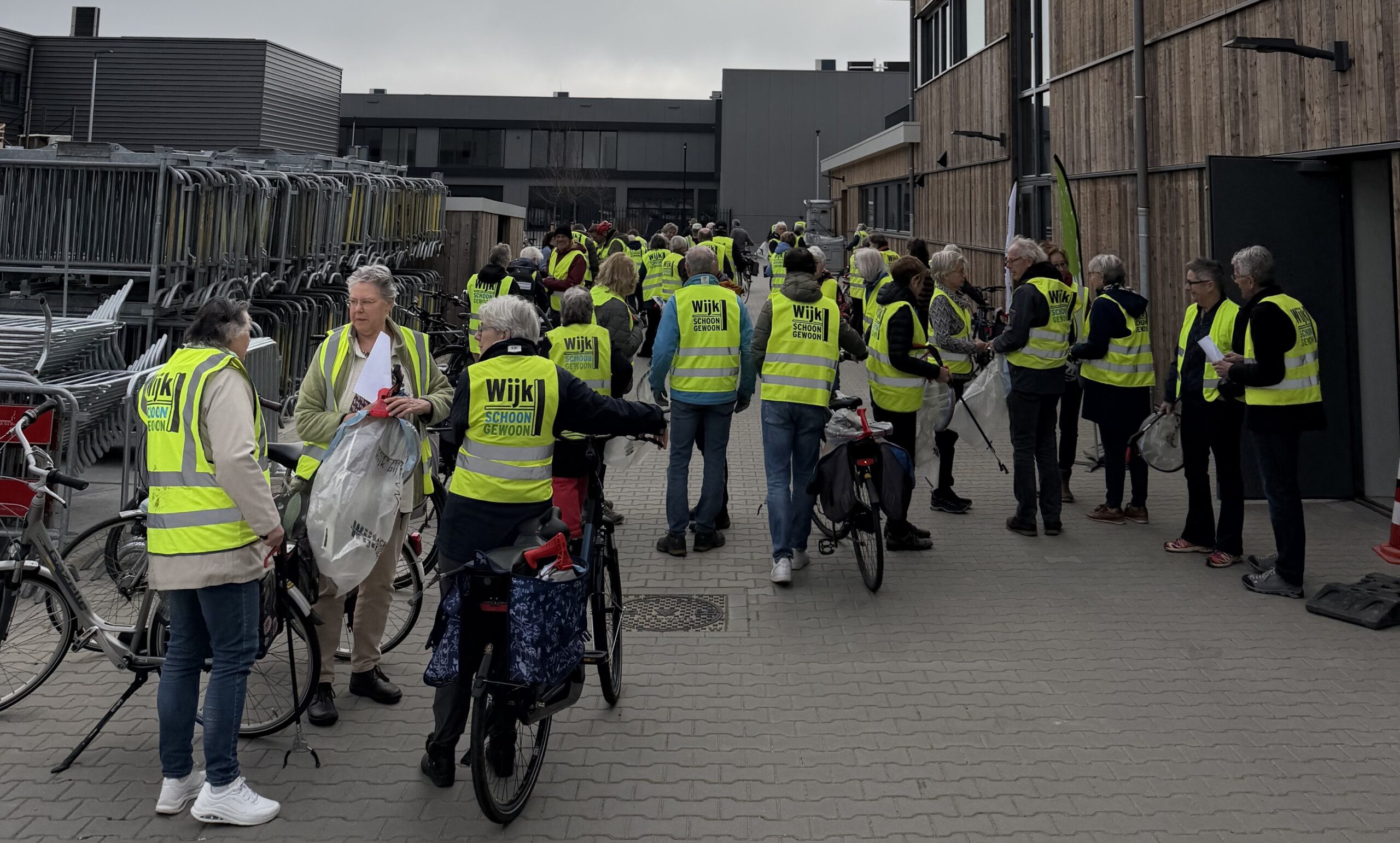 Groep mensen in gele hesjes verzamelt zich voor een schoonmaakactie, met fietsen en grijpers.