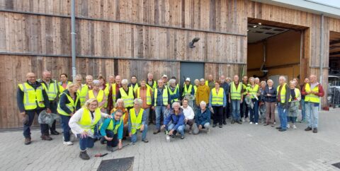 Groep mensen in gele hesjes poseert buiten voor houten gebouw.
