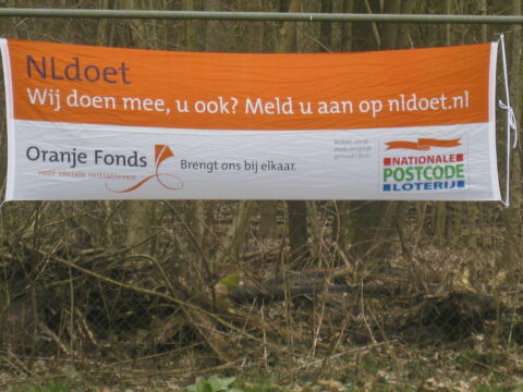 Banner van NLdoet en Oranje Fonds in een bos, uitnodigend voor deelname via nldoet.nl.