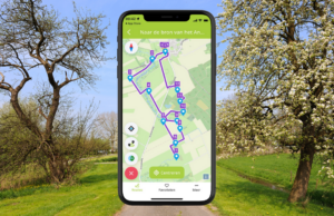 Smartphone toont een wandelroutekaart in landelijke omgeving met bomen in bloei op de achtergrond.
