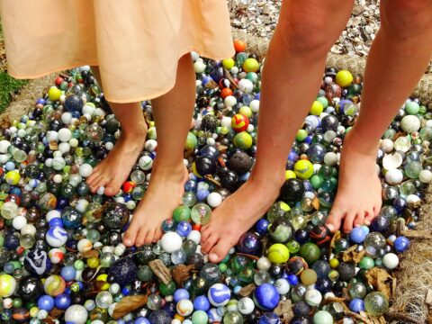 Blote voeten van twee mensen staan op een hoop kleurrijke knikkers buiten.