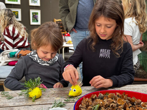 Kinderen maken knutselwerkjes met gele bolletjes en takjes aan een tafel.