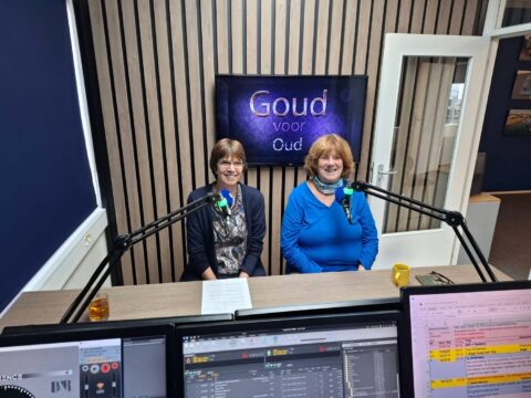 Twee vrouwen in een radiostudio met microfoons en een scherm met "Goud voor Oud".