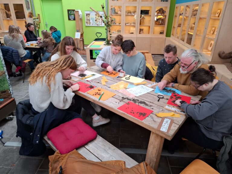 Mensen aan tafel onderzoeken objecten met loepen in een lesomgeving.
