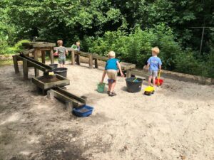 Kinderen spelen in een speeltuin met zand, watergoten en speelgoed in een groene omgeving.