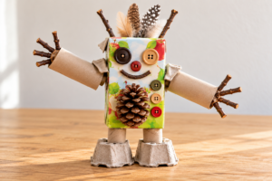 Robot gemaakt van gerecycled karton, knopen en takjes, versierd met veren.