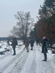 Mensen wandelen op een besneeuwd pad in een winters bos met kale bomen.