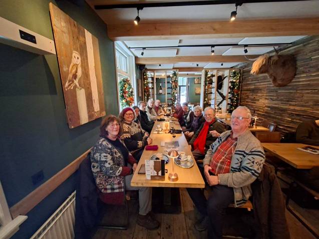 Groep oudere mensen aan een tafel in een gezellig restaurant met feestelijke decoraties.