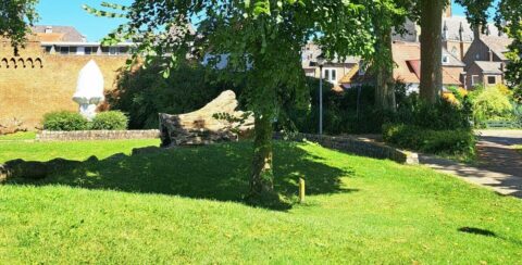Groene tuin met stenen beelden en een bakstenen muur op de achtergrond, op een zonnige dag.