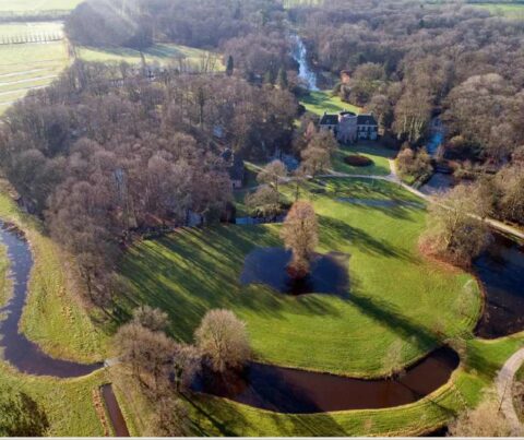 Luchtfoto van een landhuis omgeven door een bos en rivieren, met grasvelden en vijvers.