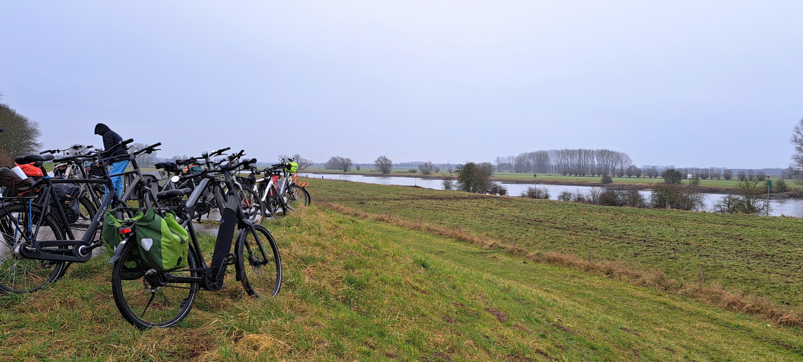Fietsen geparkeerd langs een rivierdijk met uitzicht op een wijds, groen landschap.