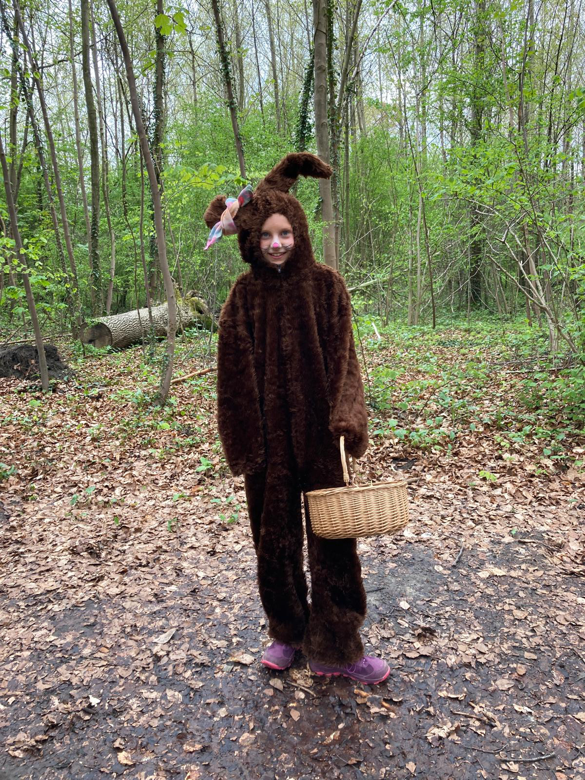 Persoon in konijnenpak met mand in bosomgeving.