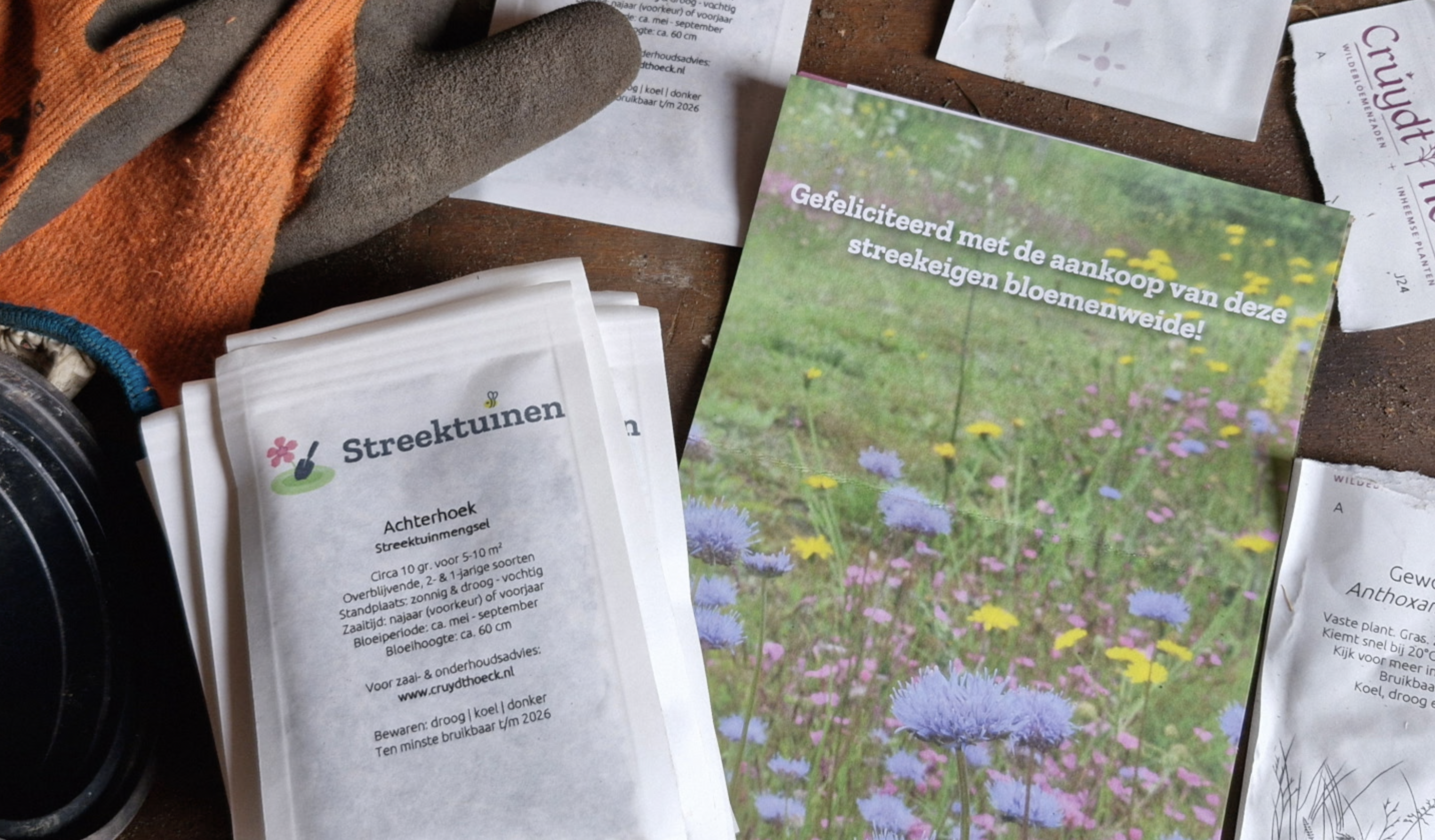 Zaden, handschoenen en een flyer met bloemenweide-afbeelding op een houten tafel.