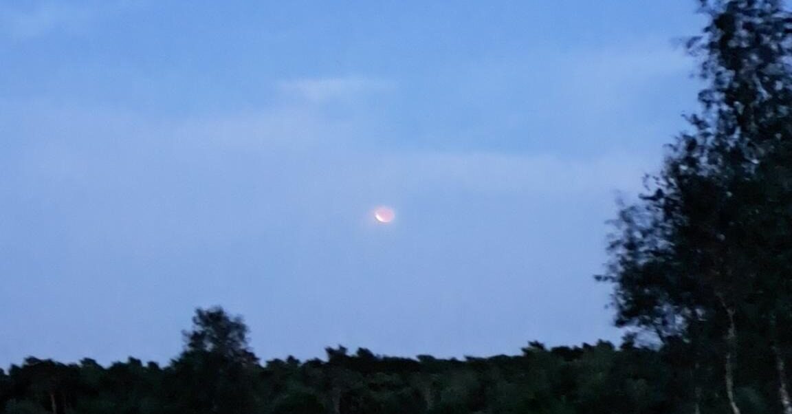 foto met open landschap waar de maansverduistering te zien is, net niet meer volledig