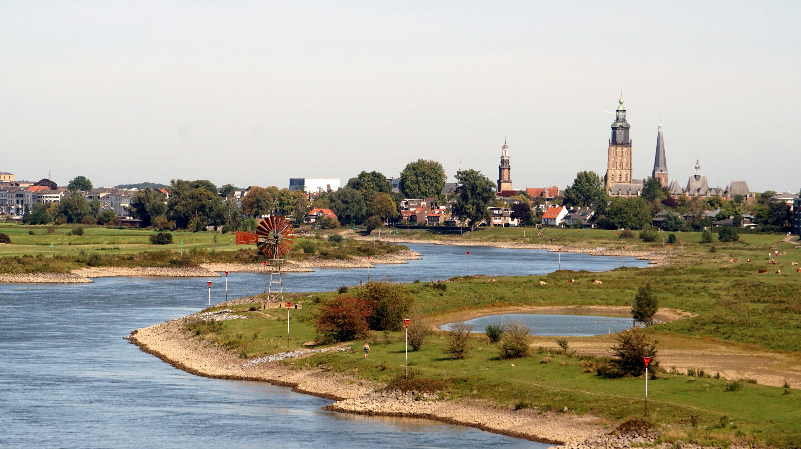 Rivierlandschap met een dorp, windmolen en kerktorens op de achtergrond.