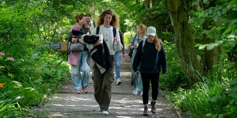 Een groep mensen wandelt op een bosrijk pad met veel groen.