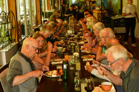 Een groep mensen eet samen aan een lange tafel in een houten restaurant.