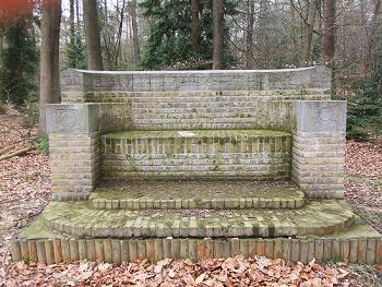 Bakstenen monument in een bos, met mos bedekte stenen en omgeven door bladeren.
