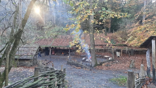 Bos met houten hutten en omheining, rook stijgt op in de herfstzon.