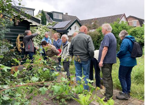 Groep mensen in een tuin naast een huis met zonnepanelen, omringd door groen.