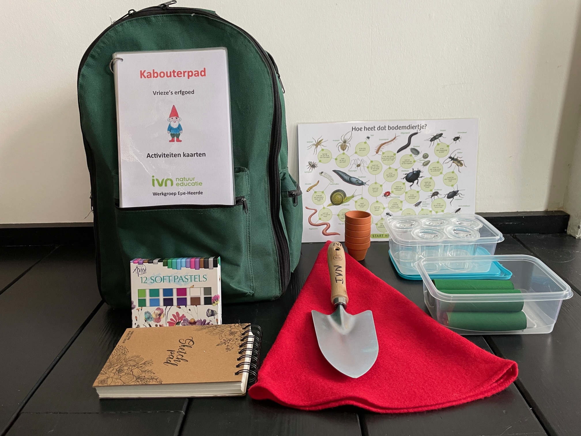 Groene rugzak met kabouterpad-activiteit, schep, notitieboek, pastelkrijtjes en bodemdiertjes-poster.