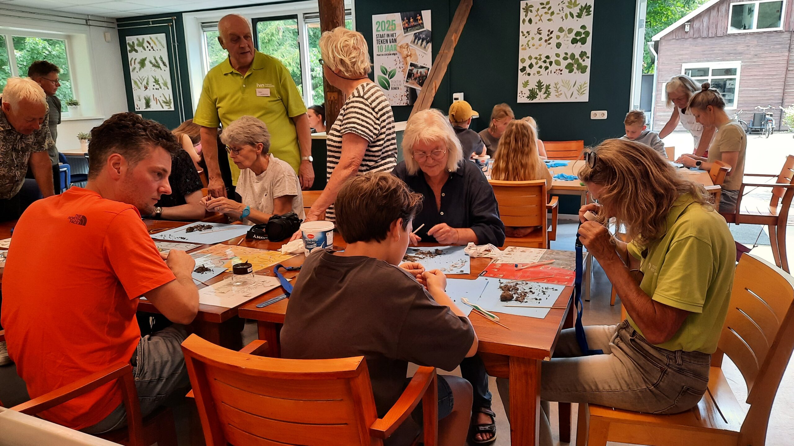 Groep mensen aan tafels, bezig met natuuronderzoek in een educatieve setting.