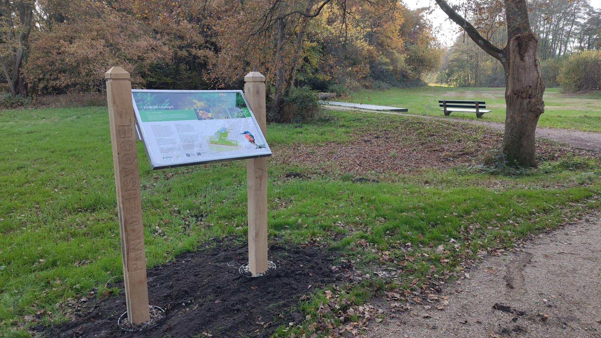 Informatiebord in een herfstachtig park met een nabijgelegen bankje en looppad.