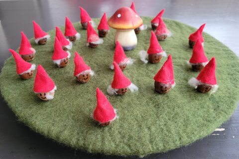 Kleine kabouters met rode hoedjes op een groene vilten ondergrond rond een paddenstoel.