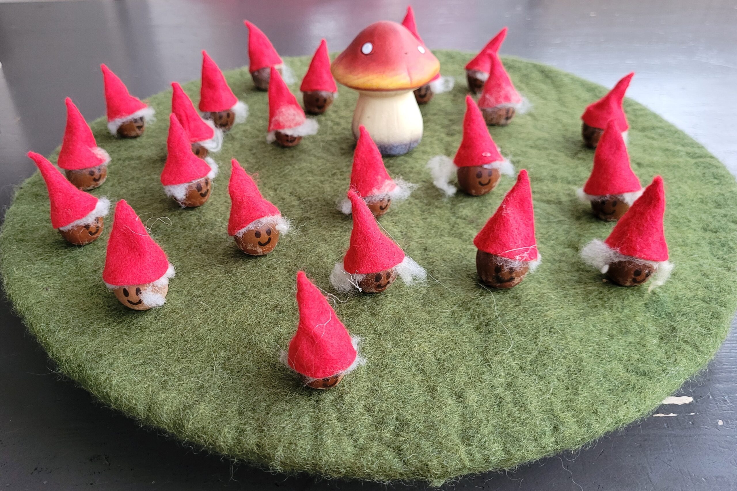Kleine kabouters met rode hoedjes op een groene vilten ondergrond rond een paddenstoel.