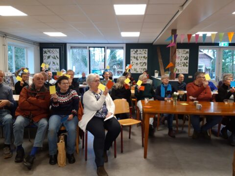 Een groep mensen in een zaal houdt gekleurde kaartjes omhoog tijdens een bijeenkomst.