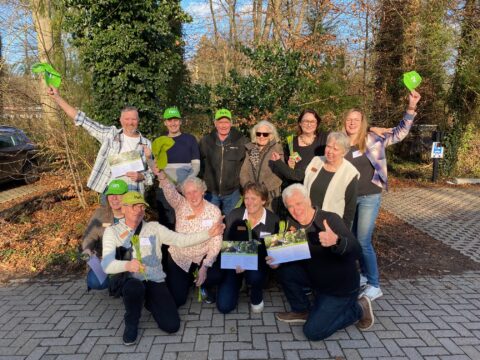 Een groep mensen poseert buiten met groene petten en certificaten, ze zien er blij uit.