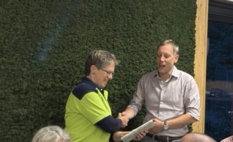 Twee mannen schudden handen voor een moswand, één in bedrijfskleding.