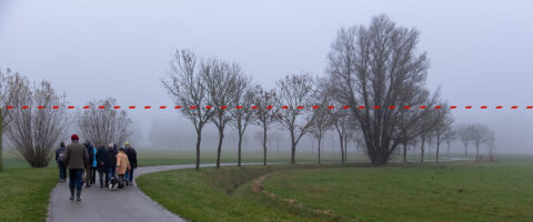 Groep wandelaars op een mistig pad tussen bomen, met rode stippellijn boven hen.