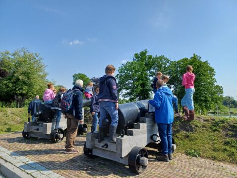 Groep mensen bij twee historische kanonnen in een park, onder een heldere, blauwe lucht.