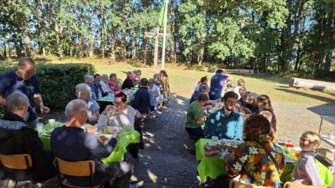 Mensen aan lange tafels aan een bosrand