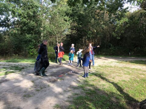 Groep mensen in het bos, sommigen kijken naar een vrouw die iets aanwijst.