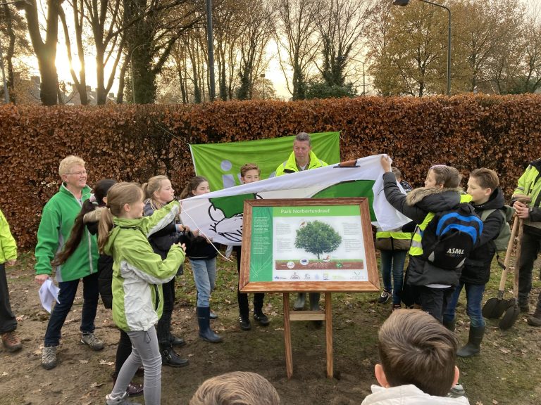 Groep mensen onthult een informatiebord in een park, omringd door herfstbladeren.