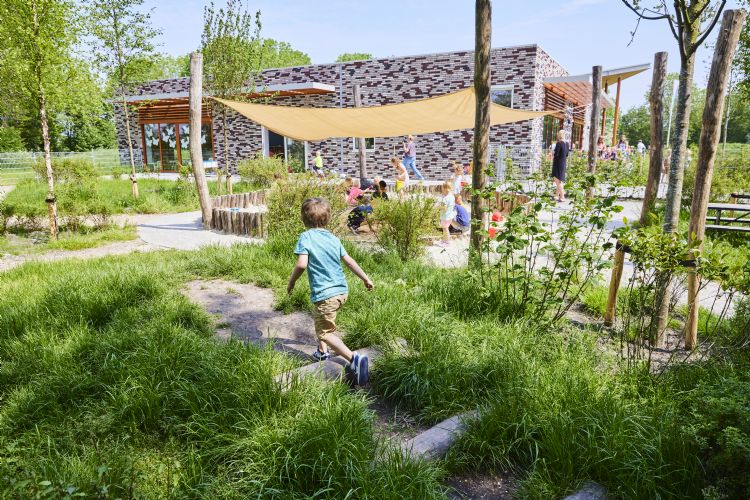 Kinderen spelen buiten in een groene tuin voor een modern gebouw met zonwering.