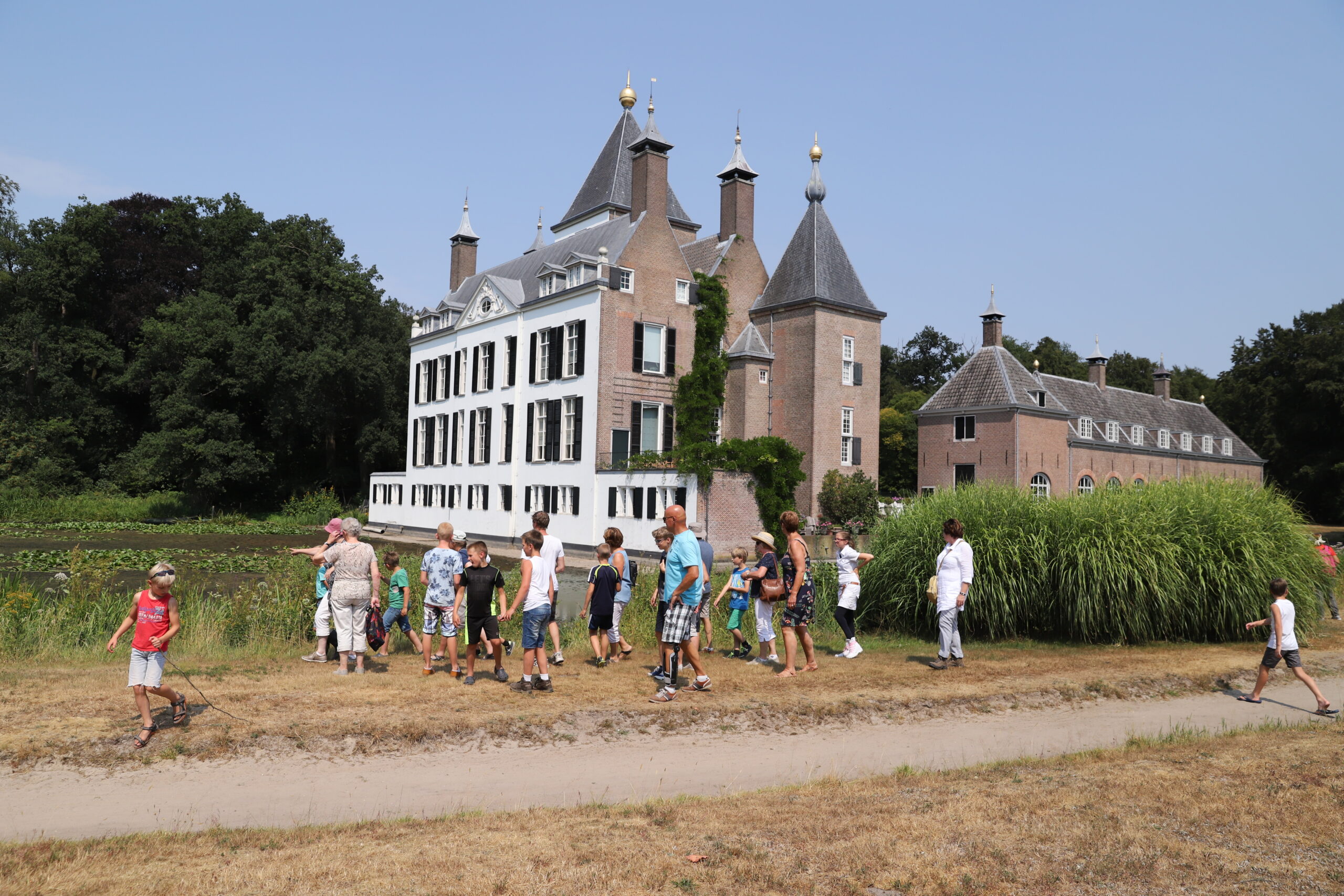 Kinderen wandelen met volwassenen voor een historisch kasteel op een zonnige dag.