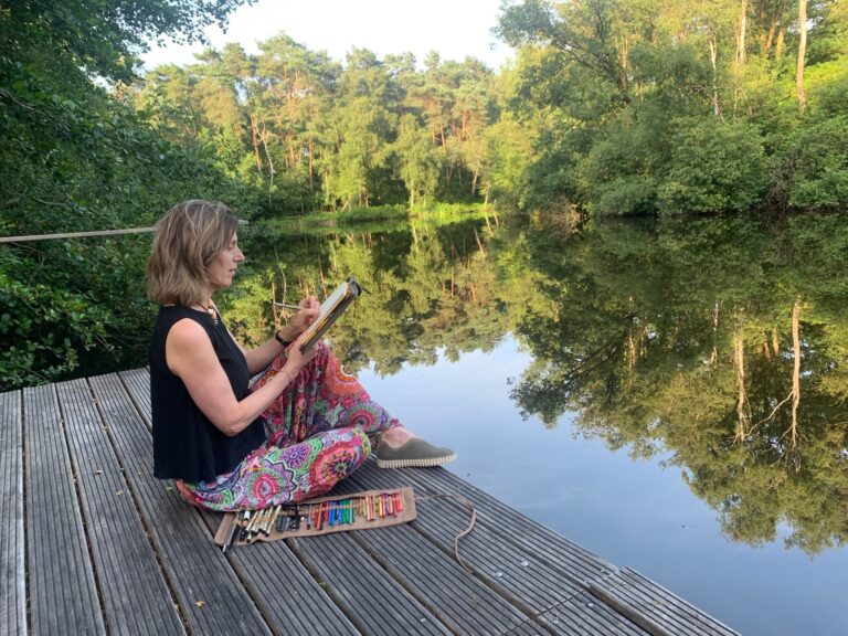 Vrouw tekent aan waterkant, omgeven door bomen en serene natuur.