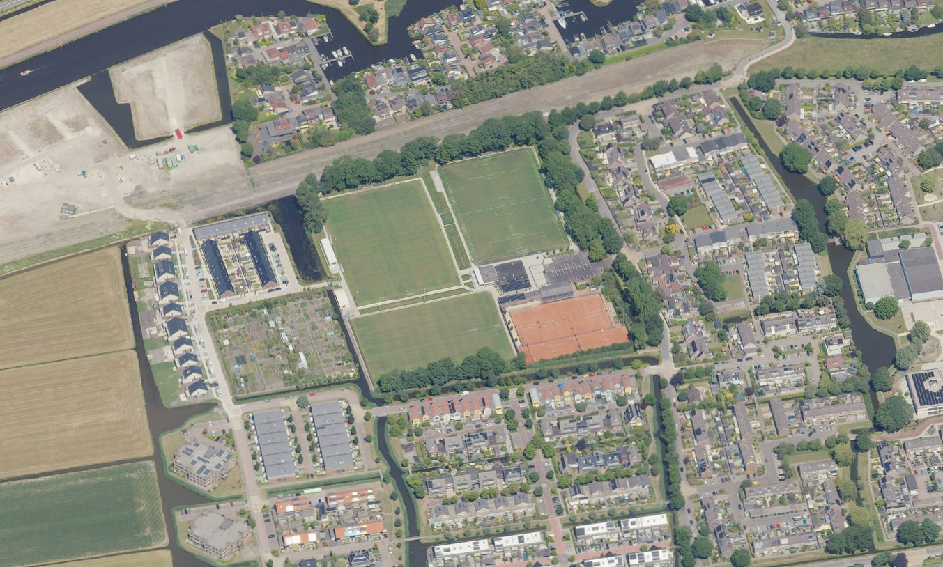 Luchtfoto van een woonwijk met voetbalvelden, tennisbanen en omringende waterwegen.