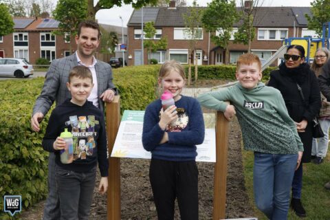 Groep mensen buiten bij een informatiebord in een speeltuin met een groene omgeving.