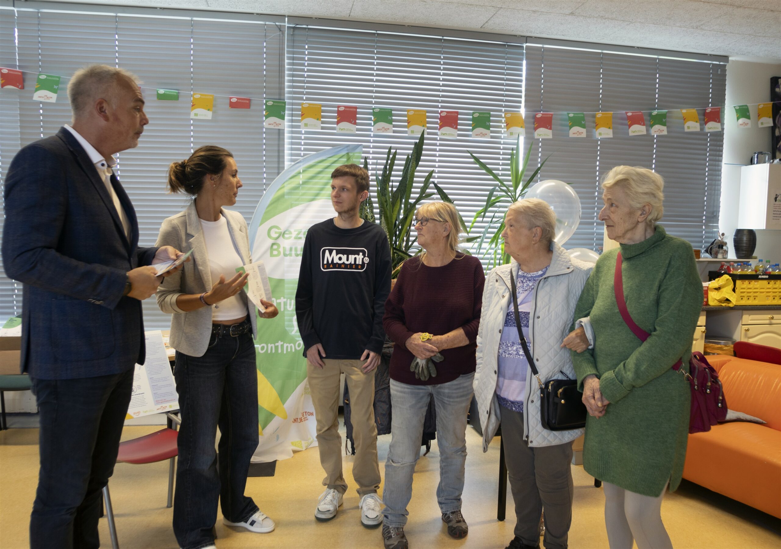 Groep mensen in gesprek in een gemeenschapsruimte met een banner op de achtergrond.