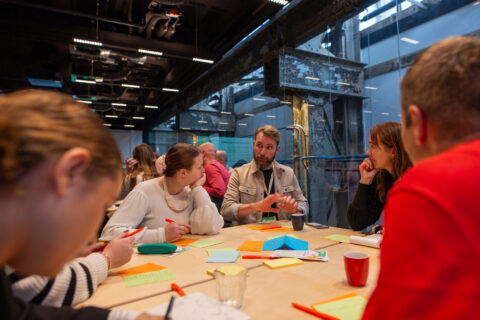 Groep mensen overlegt rond tafel met kleurrijke notities en pennen in moderne ruimte.
