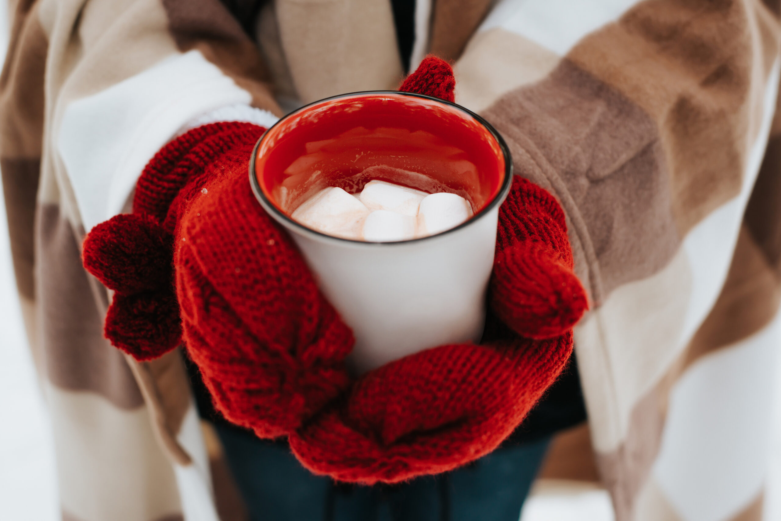 Rode handschoenen houden een mok chocolademelk met marshmallows vast.