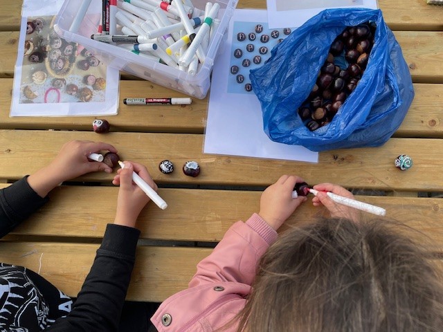 Twee kinderen versieren kastanjes met stiften aan een houten tafel buiten.