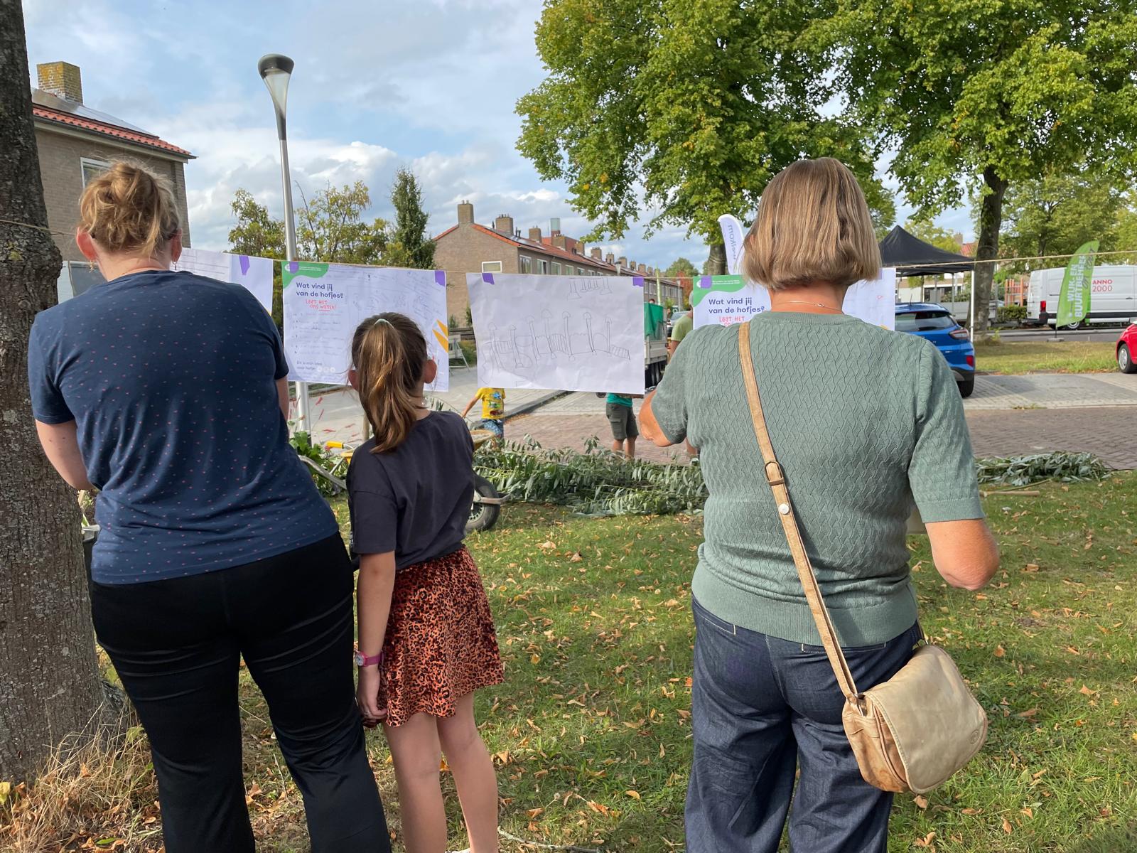Mensen bekijken tekeningen die aan een lijn hangen in een parkachtige omgeving.